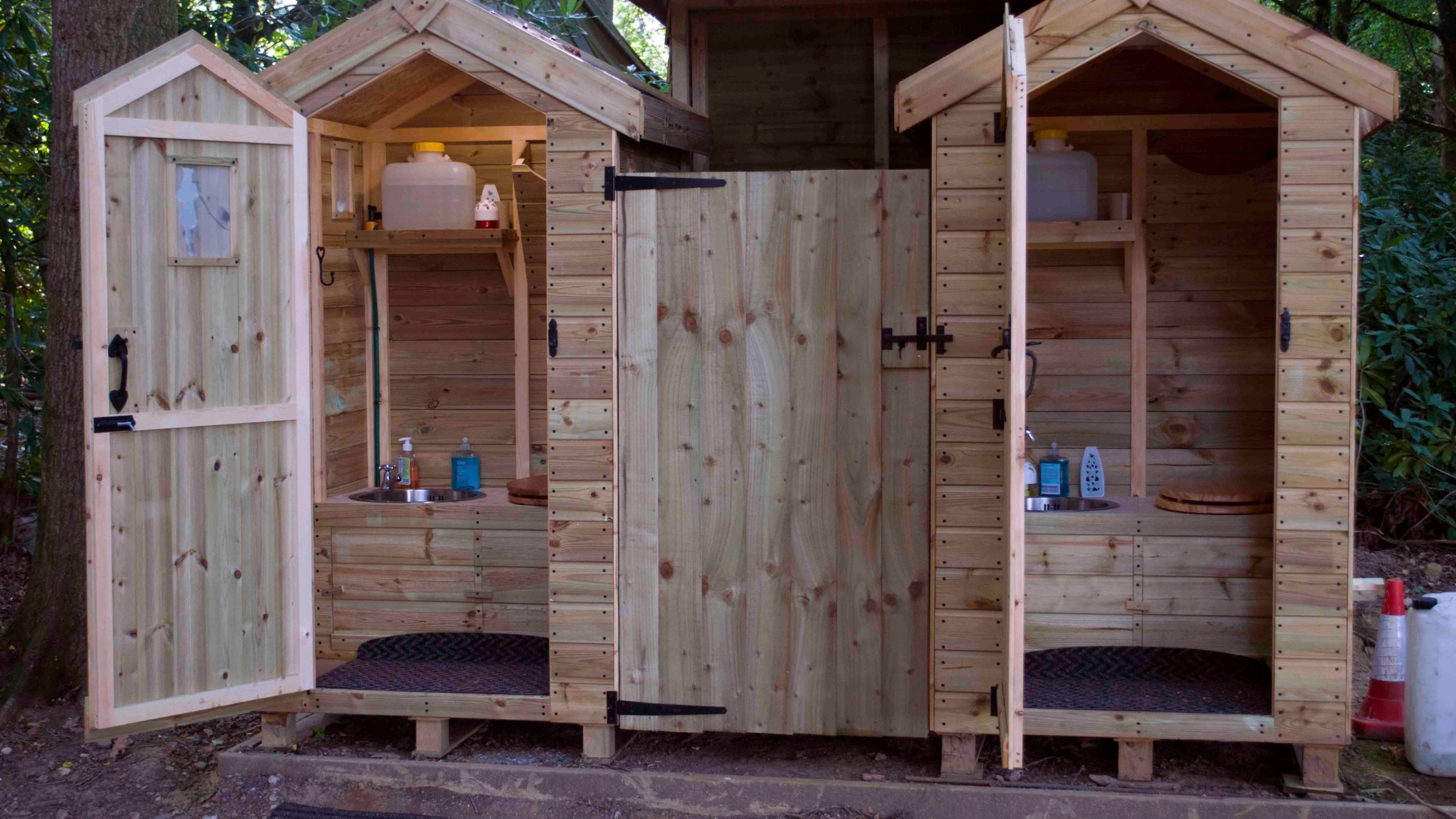 Wooden outdoor toilet sheds with open doors and various supplies inside.