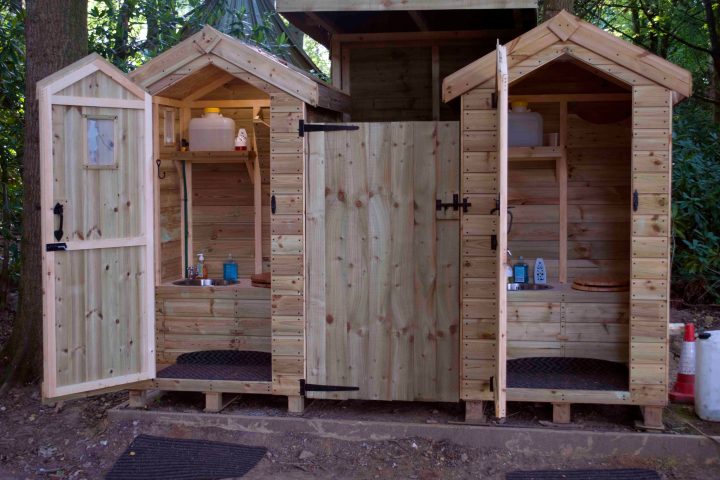 Wooden outdoor toilet sheds with open doors and various supplies inside.