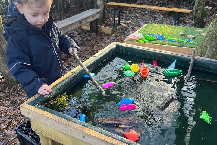 Child playing with toy boats and animals in outdoor water table.