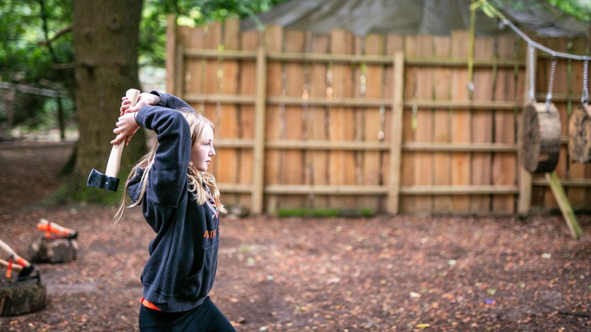 Person swinging an axe in a wooded area with a wooden fence in the background.