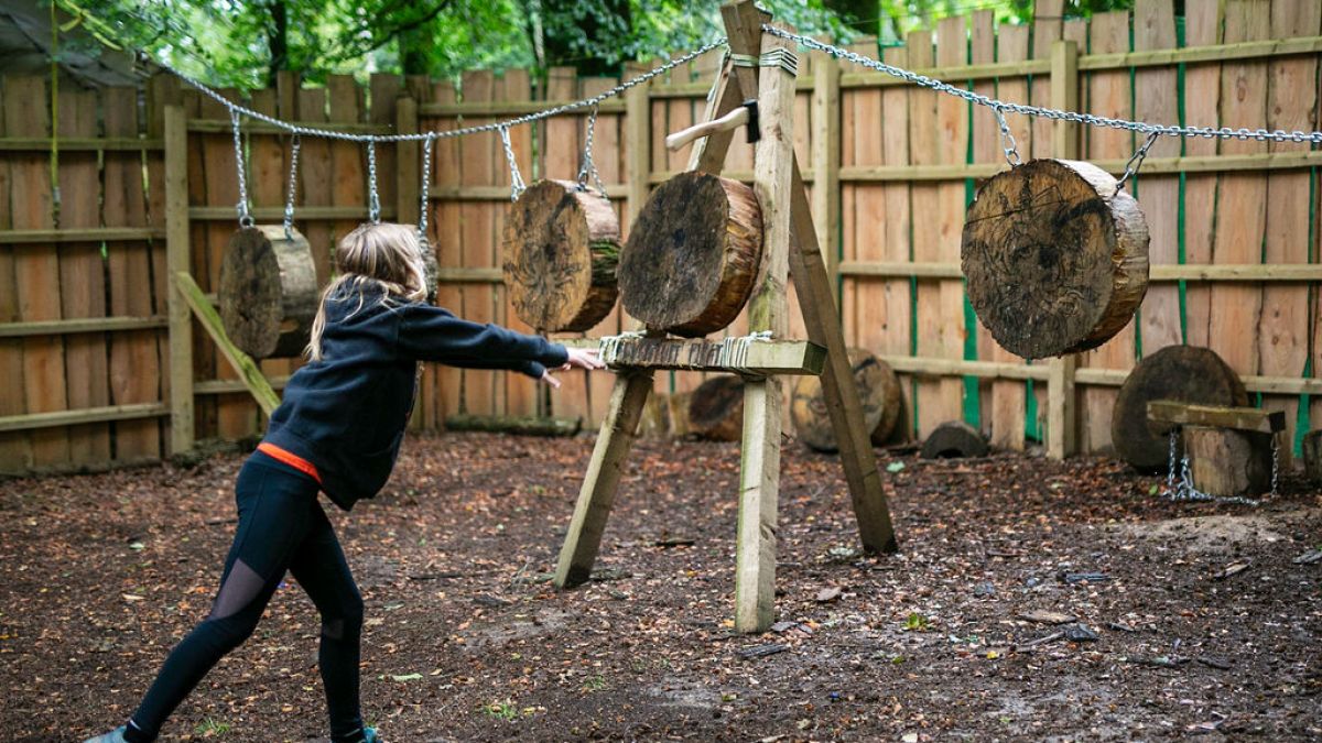 Child throwing a small axe at wooden targets in an outdoor setting.