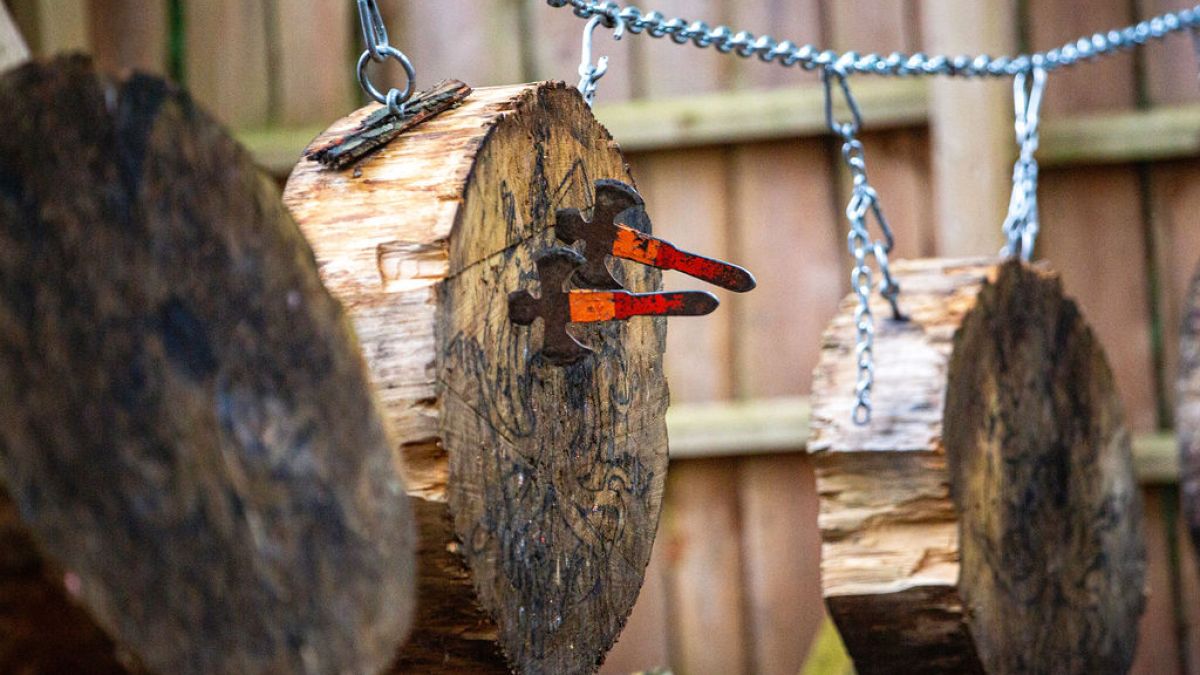 Axe heads embedded in hanging wooden logs via chains.