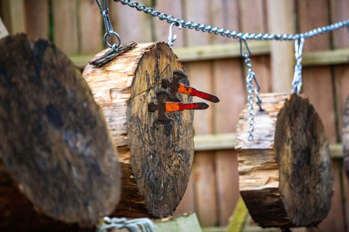 Axe heads embedded in hanging wooden logs via chains.
