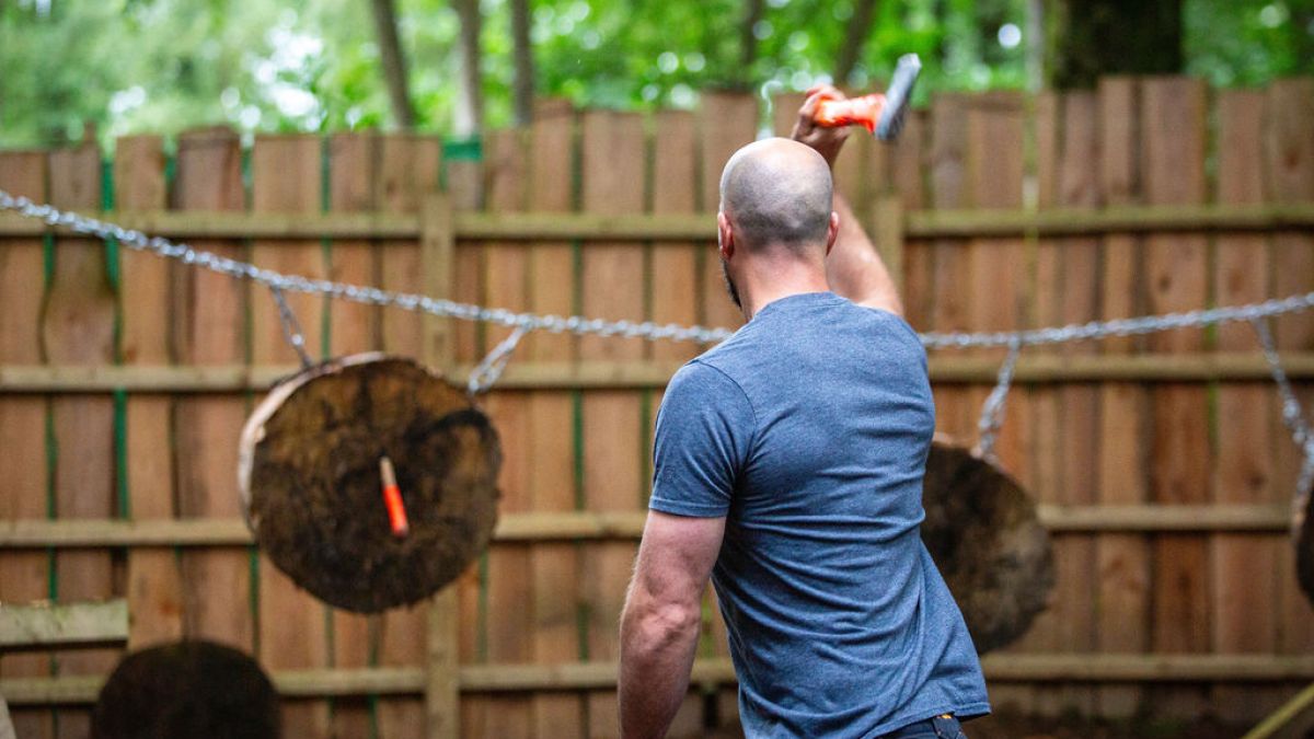 Man throwing an axe at wooden targets in an outdoor setting.