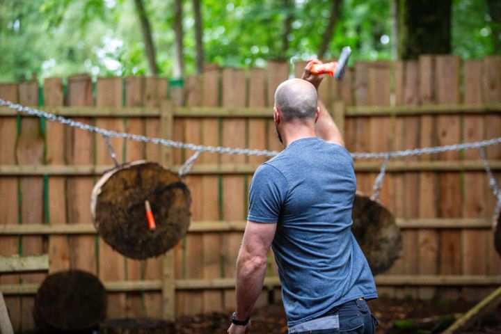 Man throwing an axe at wooden targets in an outdoor setting.
