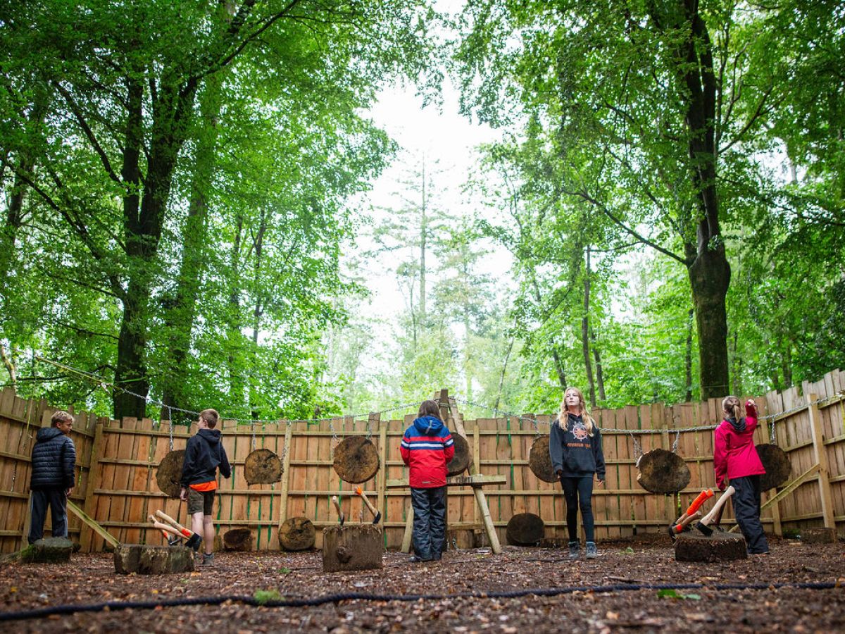 Children in a wooded area practicing axe throwing at wooden targets.
