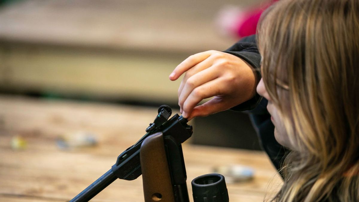 Child loading a pellet into an air rifle at a wooden table.