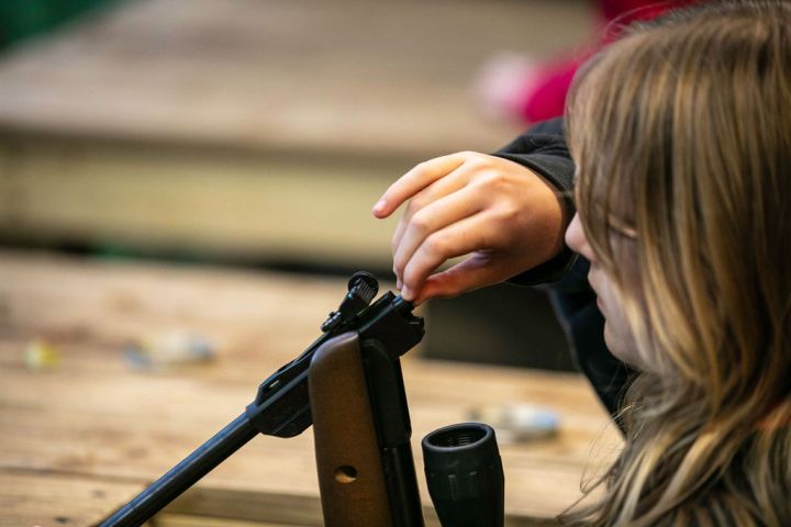 Child loading a pellet into an air rifle at a wooden table.