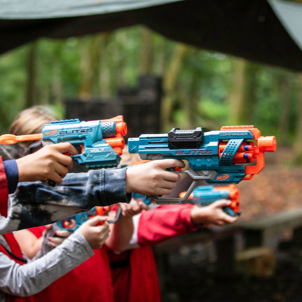 Children aiming colorful toy dart guns in a forest setting.