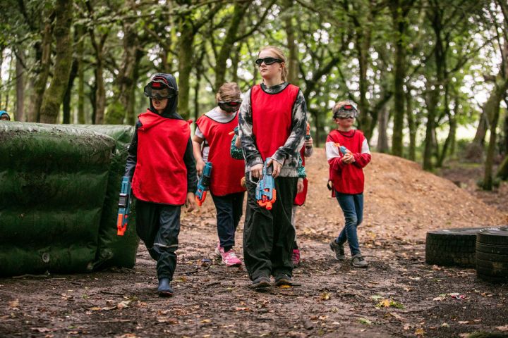 Children in red vests holding toy guns in a forest setting.