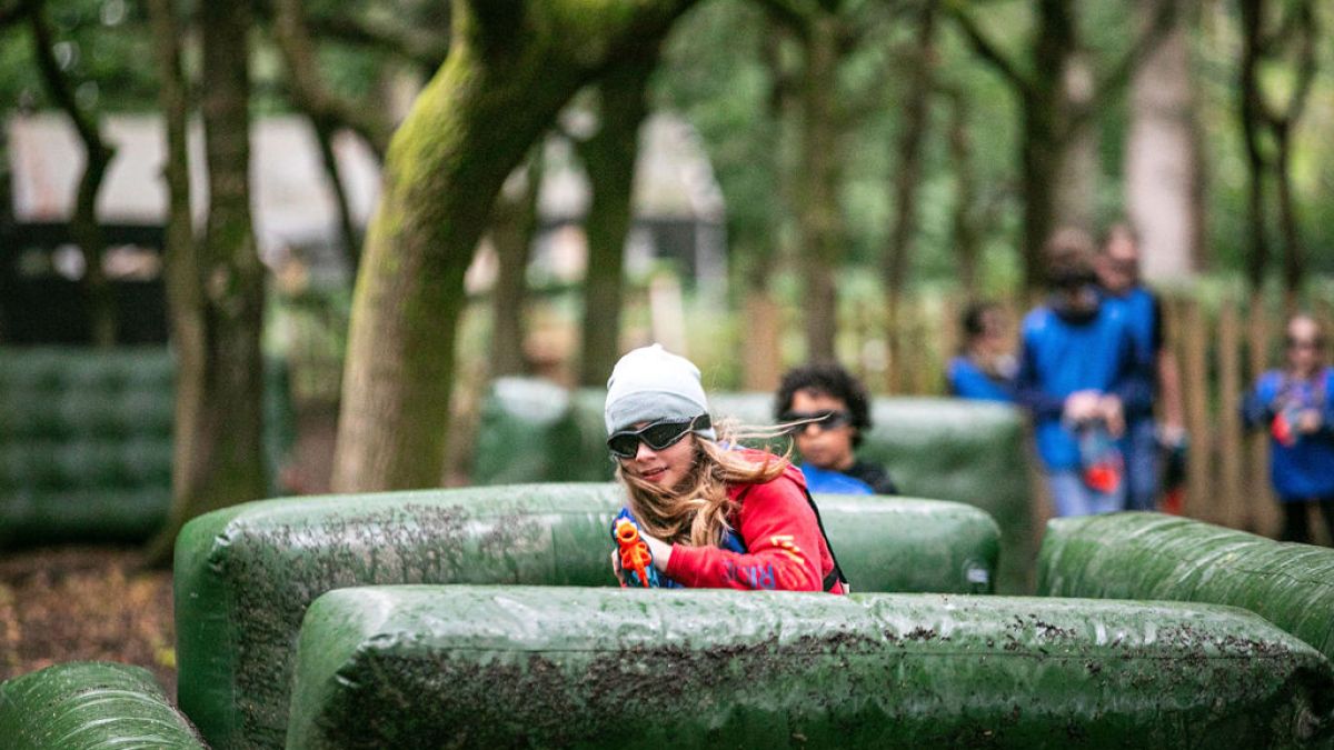 People playing a laser tag game in a forest with inflatable barriers and trees.