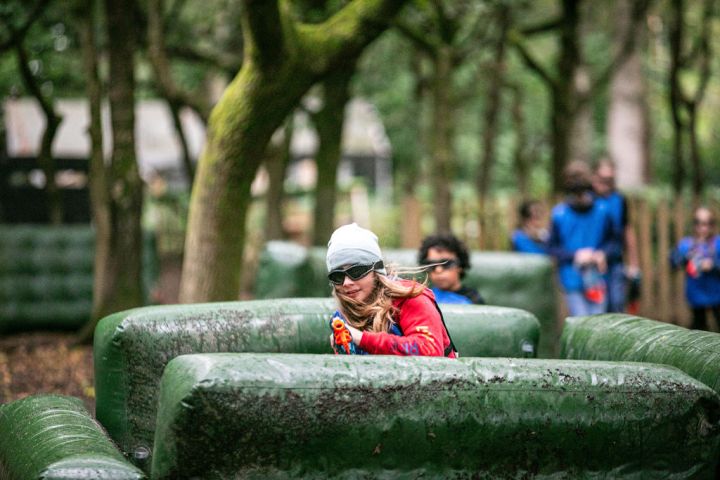 People playing a laser tag game in a forest with inflatable barriers and trees.
