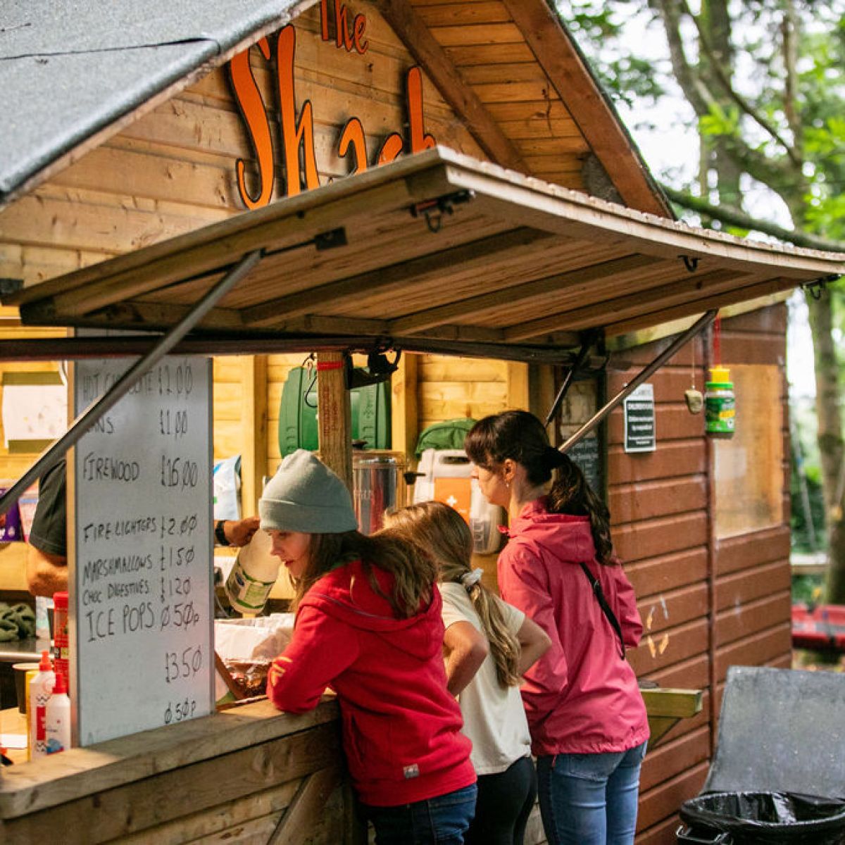 People ordering at a small wooden shack in a forested area.