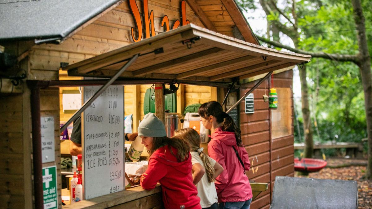 People ordering at a small wooden shack in a forested area.