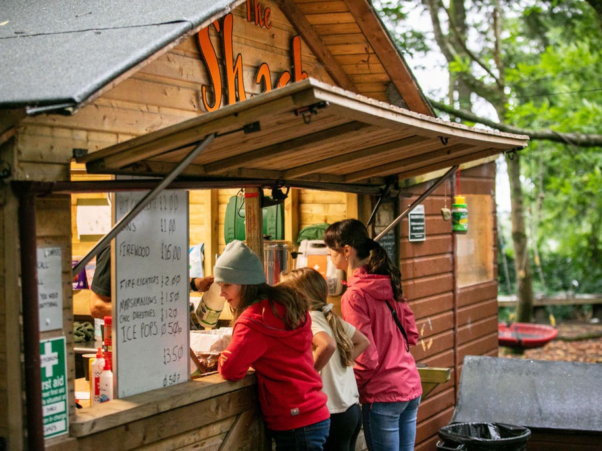 People ordering at a small wooden shack in a forested area.
