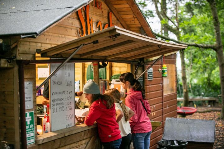 People ordering at a small wooden shack in a forested area.