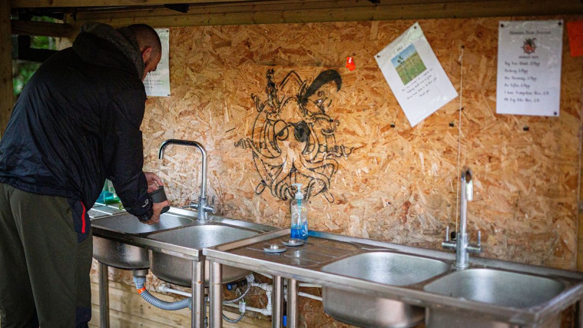Person using outdoor sink with wooden wall backdrop featuring art and papers.