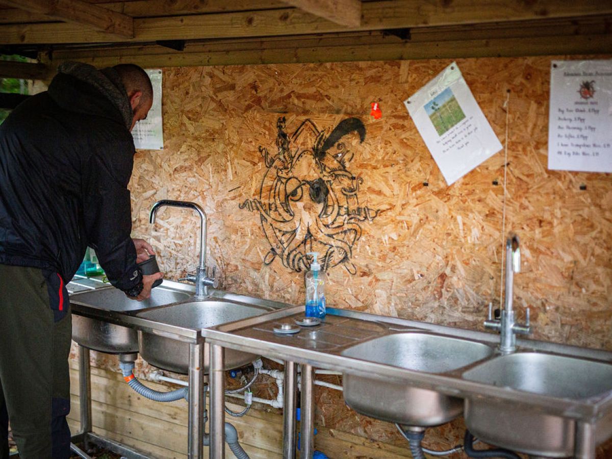 Person using outdoor sink with wooden wall backdrop featuring art and papers.