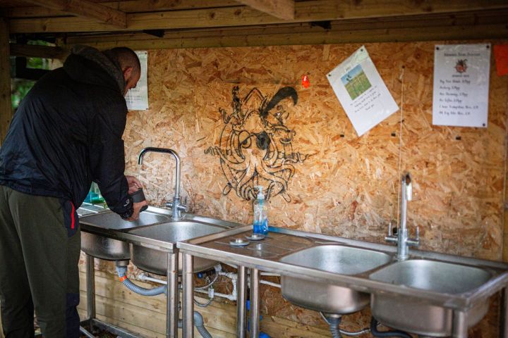 Person using outdoor sink with wooden wall backdrop featuring art and papers.