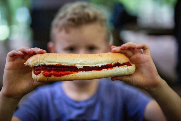 Child holding a hot dog with ketchup, face blurred in the background.