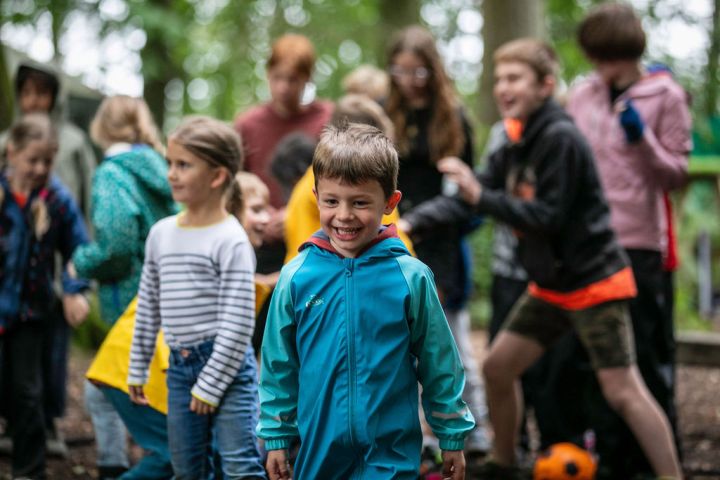 Children playing outdoors, boy in blue jacket smiling in foreground.