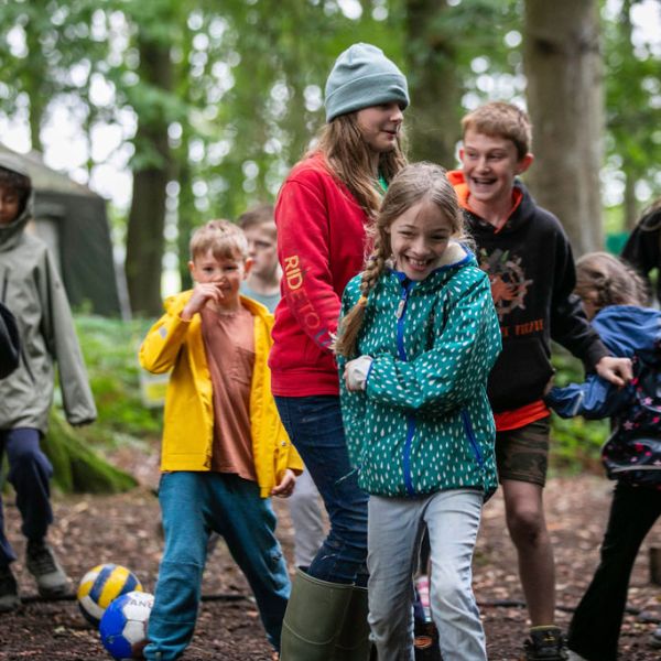 Group of kids playing in a forest campsite with a colorful ball.