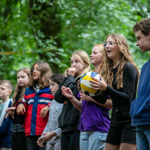 Group of kids standing outdoors, one holding a volleyball.