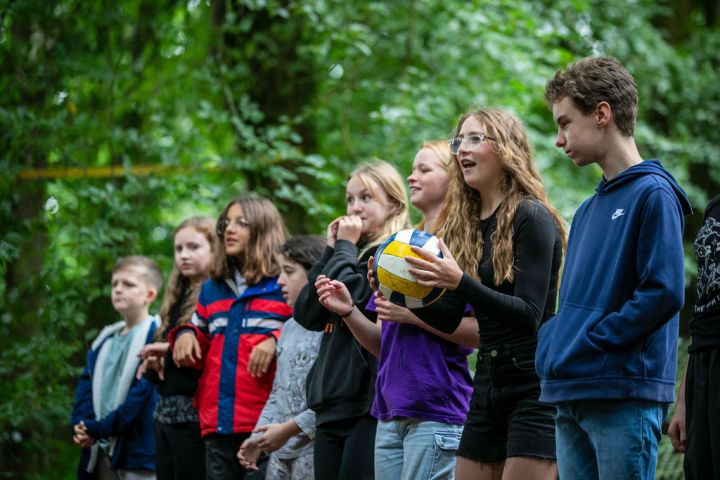 Group of kids standing outdoors, one holding a volleyball.