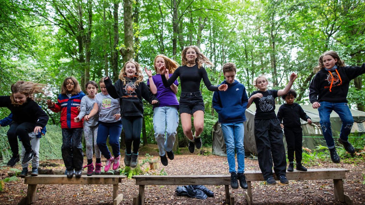 Children jumping off benches in a forest setting.