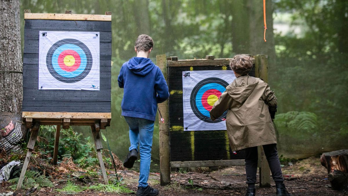 Two children checking archery targets in a forest setting.