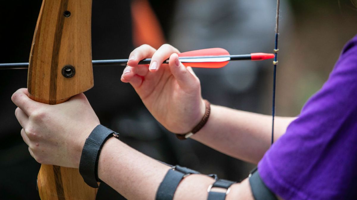 Close-up of a person preparing to shoot an arrow with a wooden bow.