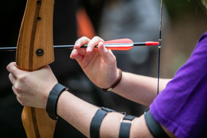 Close-up of a person preparing to shoot an arrow with a wooden bow.