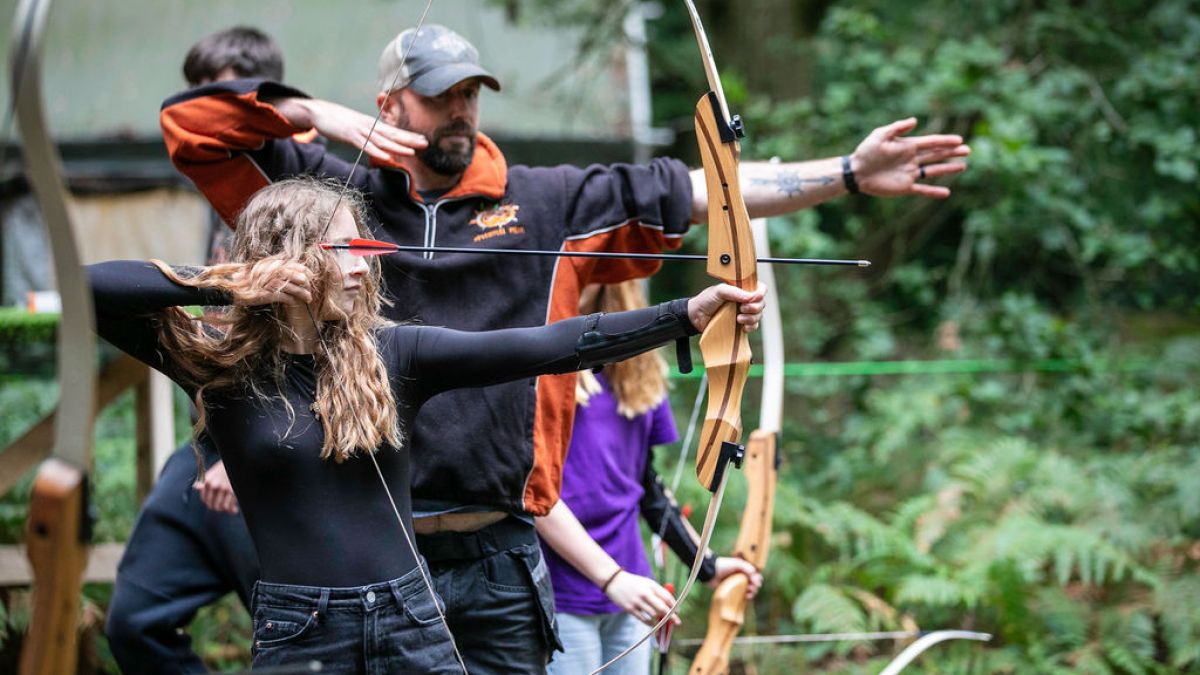 People aiming bows and arrows in an outdoor archery activity.
