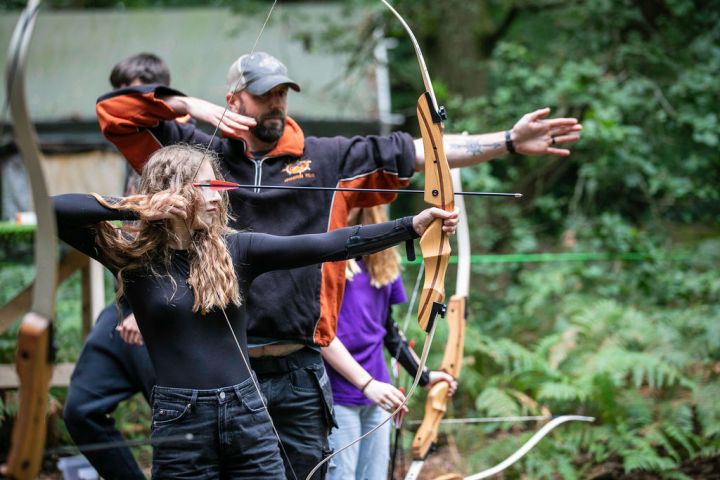 People aiming bows and arrows in an outdoor archery activity.