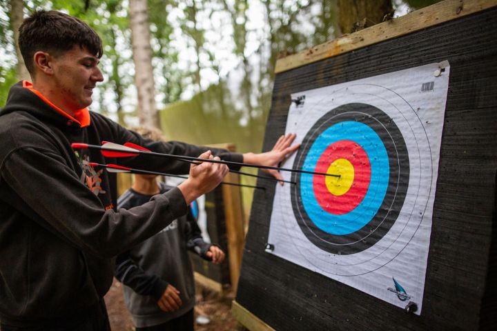 A person retrieves arrows from a target in an outdoor archery range.