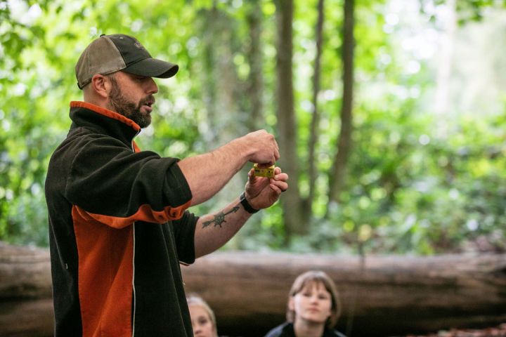 Man outdoors demonstrating with small object, children watching.