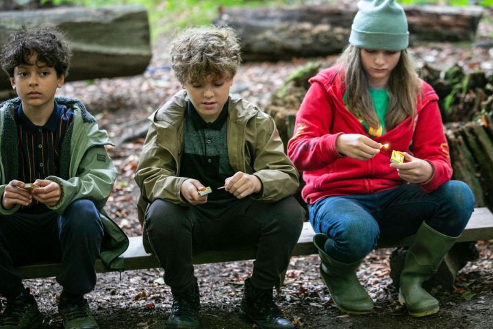 Three children sitting outside on a bench, holding and examining objects.