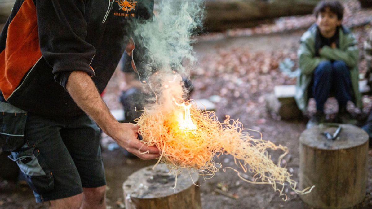 Person demonstrating fire-starting with tinder in an outdoor setting, smoke rising.