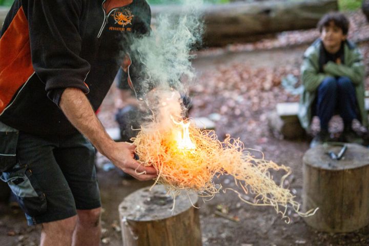 Person demonstrating fire-starting with tinder in an outdoor setting, smoke rising.