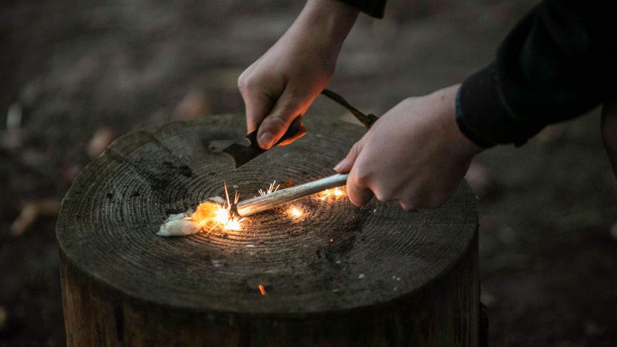 Hands creating sparks with a fire starter on a tree stump.