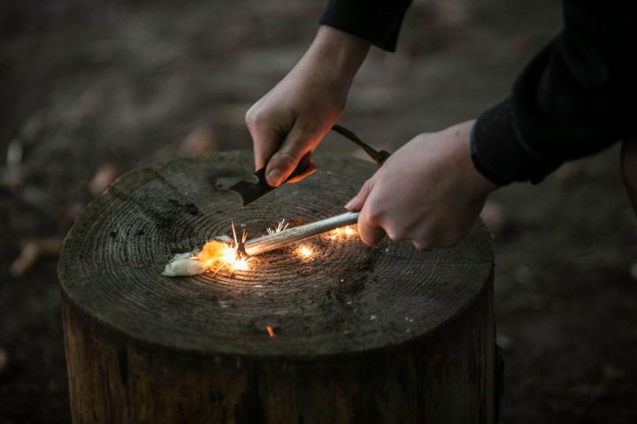 Hands using a flint and steel to create sparks on a tree stump.