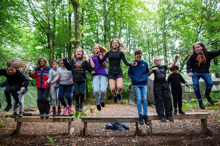 Group of kids jumping off benches in a forest setting.