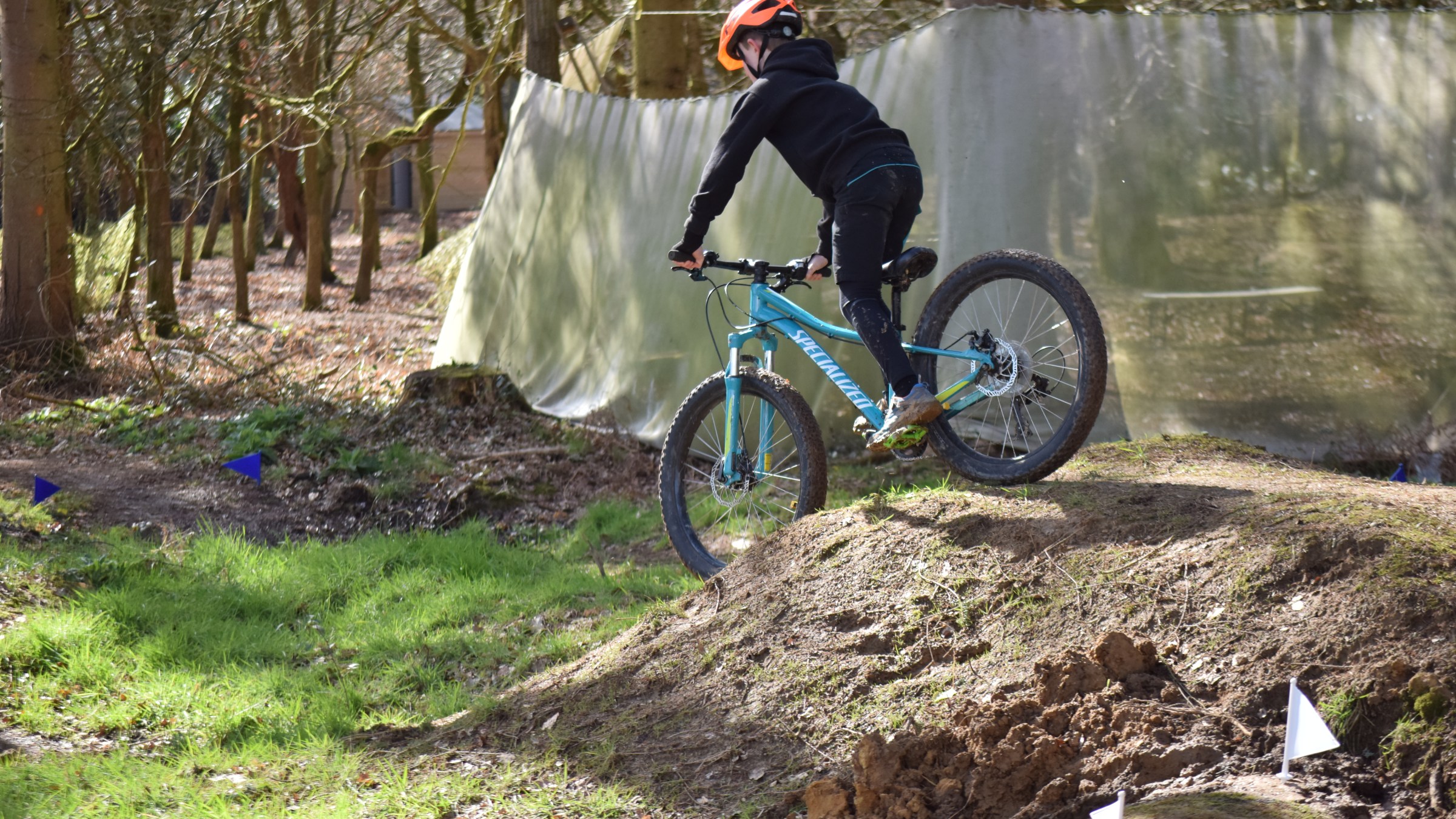 Person in orange helmet riding a blue mountain bike on a dirt trail in a forest.