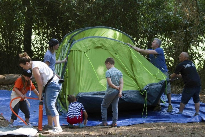 Group of people setting up a green tent in a wooded area on a blue tarp.