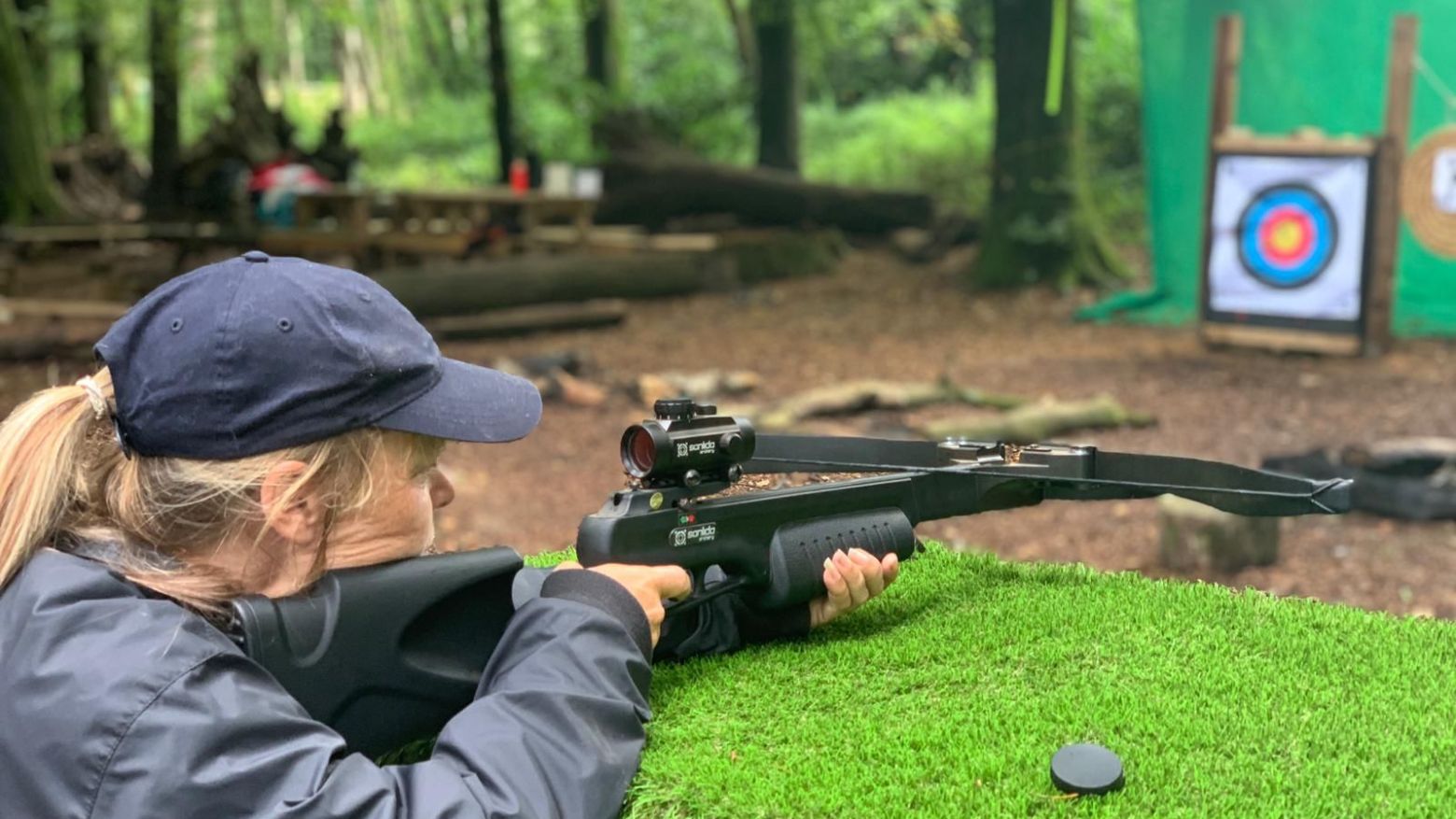 Person aiming a crossbow at a target in a wooded area.