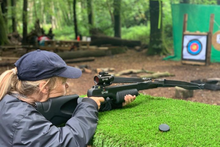 Person aiming a crossbow at a target in a wooded area.