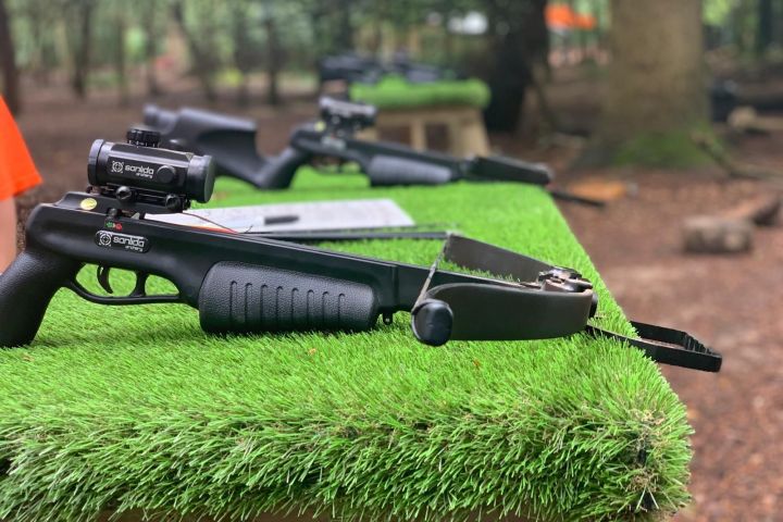Crossbow on a table with artificial grass outdoors near trees.