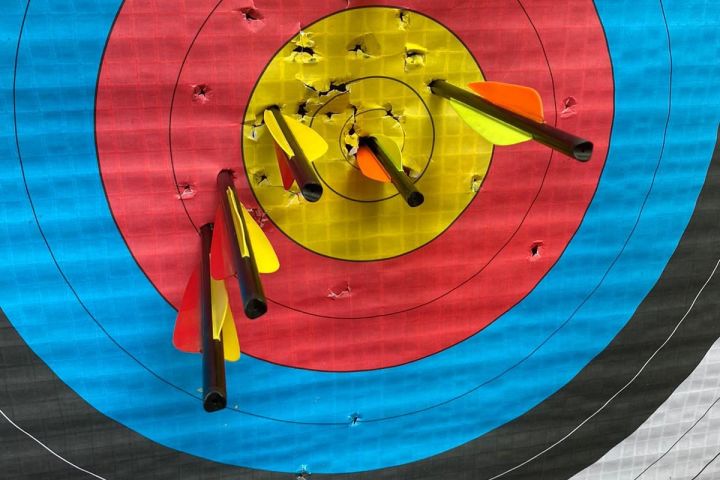 Archery target with multiple arrows hitting the yellow center area.