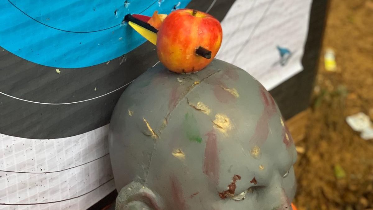Apple with arrow on target, mounted on mannequin head near bullseye.