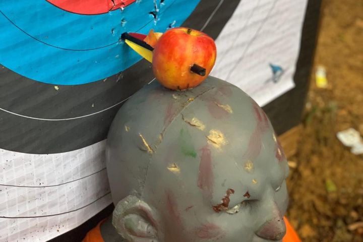 Apple with arrow on target, mounted on mannequin head near bullseye.